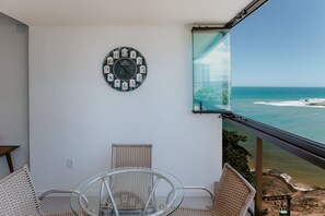 A balcony with wicker chairs, a glass table, and a wall clock.