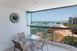 A balcony with a glass table and wicker chairs, overlooking a beach and ocean.