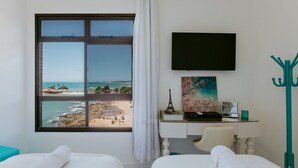 Habitación de hotel con dos camas, un escritorio con computadora, televisión y vista a la playa.