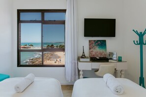 A hotel room with two beds, a desk with a computer, a TV, and a view of the beach.