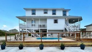 Ein zweistöckiges Haus mit Pool, Holzterrasse und Kübelpflanzen.