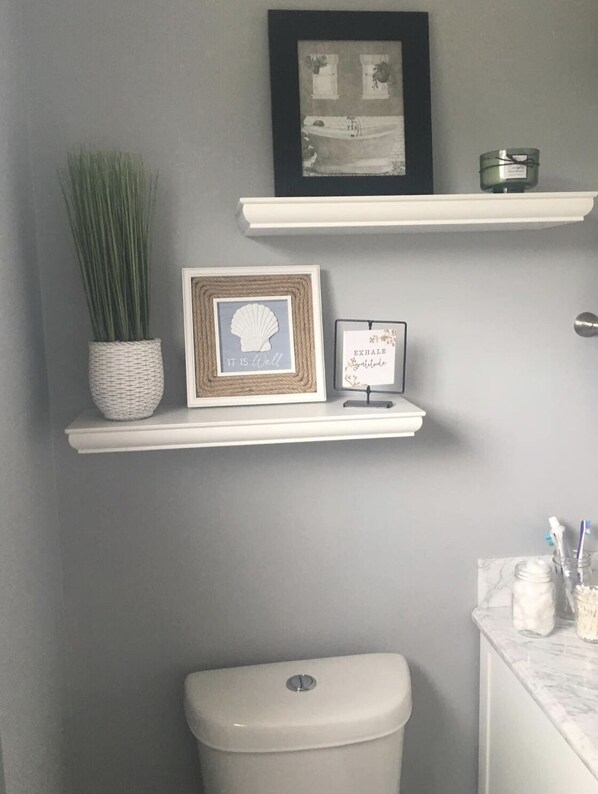 A bathroom with a toilet, a sink, and two shelves with decorative items.