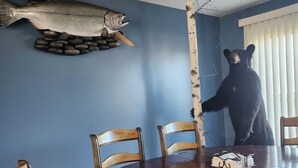 Comedor con una mesa de madera, sillas, una decoración de pescado, un ventilador de techo y una estatua de oso.
