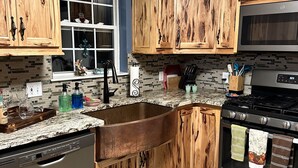 Una cocina con armarios de madera, un lavamanos de acero inoxidable, lavavajillas, estufa y ventana con vistas.