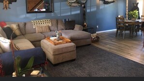 Una sala de estar con un sofá modular, un reposapiés y una zona de comedor con mesa y sillas.