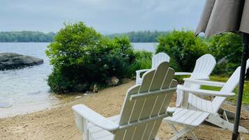 Relax in Adirondack chairs on the sandy beach, overlooking the serene lake and lush green surroundings.