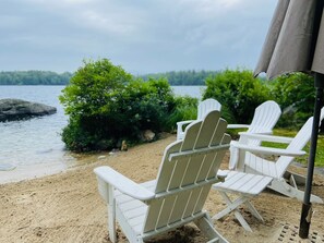 Relax in Adirondack chairs on the sandy beach, overlooking the serene lake and lush green surroundings.