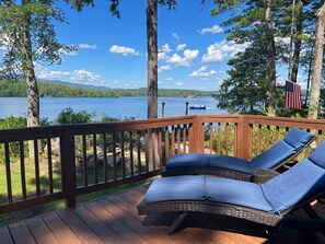 Relax on the deck with a serene lake view and forest surroundings, featuring two comfortable lounge chairs.