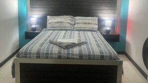 A bed with a striped bedspread, two bedside tables with lamps, and a wall-mounted air conditioner. - Townhouse426 gated community (Portmore)