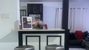 A kitchen area with a bar counter, two stools, a refrigerator, and a sink. - Townhouse426 gated community (Portmore)