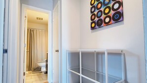 A hallway with a white door leading to a bathroom, a white metal shelving unit, and a wall-mounted vinyl record art piece. - Stylish & Central - Walk to UK Campus/Hospital, Mins to DT/Rupp/Keeneland (Lexington)