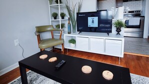 A modern living room with a black coffee table, a TV, and a white entertainment unit. - Stylish & Central - Walk to UK Campus/Hospital, Mins to DT/Rupp/Keeneland (Lexington)