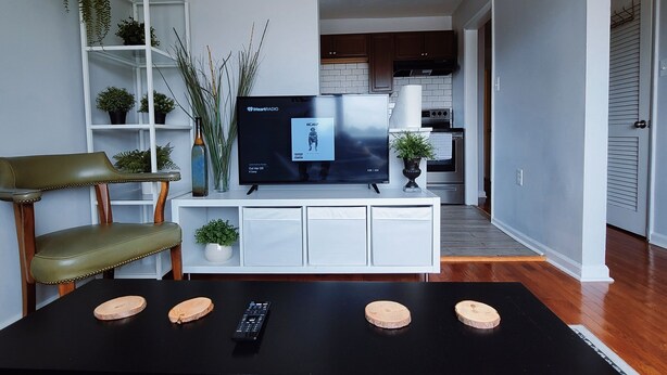 A modern living room with a black coffee table, a television, and a white entertainment unit. - Stylish & Central - Walk to UK Campus/Hospital, Mins to DT/Rupp/Keeneland (Lexington)