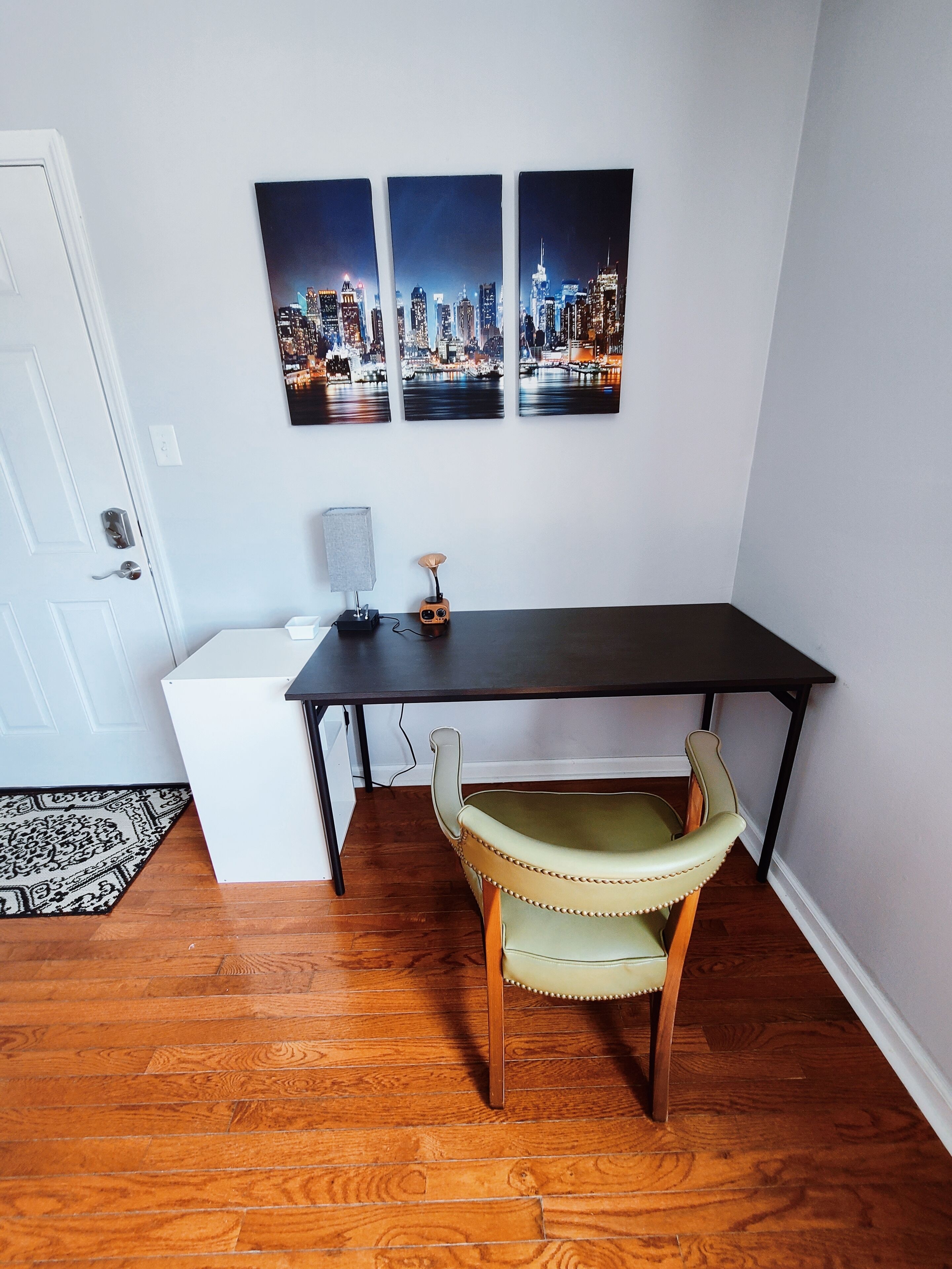 A room with a desk, a chair, and three cityscape paintings on the wall.