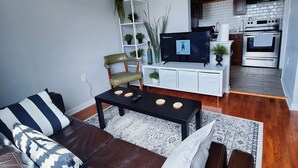 A modern living room with a leather sofa, a coffee table, and a TV. There is a kitchen area with a stove and cabinets in the background. - Stylish & Central - Walk to UK Campus/Hospital, Mins to DT/Rupp/Keeneland (Lexington)