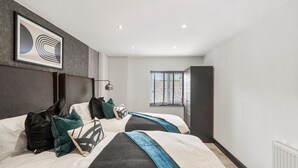 A modern bedroom with two beds, a large abstract painting, and a window with blinds. - Stunning Coastal Retreat - Indoor Pool - Sauna (Hunmanby)