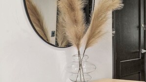 A round mirror on a wall, a clear glass vase with pampas grass on a wooden console table, and a dark door in the background. - Stunning Coastal Retreat - Indoor Pool - Sauna (Hunmanby)