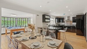A modern kitchen with dark cabinetry, a central island, and a dining area with a long table set for six. - Stunning Coastal Retreat - Indoor Pool - Sauna (Hunmanby)