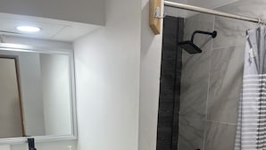 Un baño con lavamanos blanco, espejo y zona de ducha.