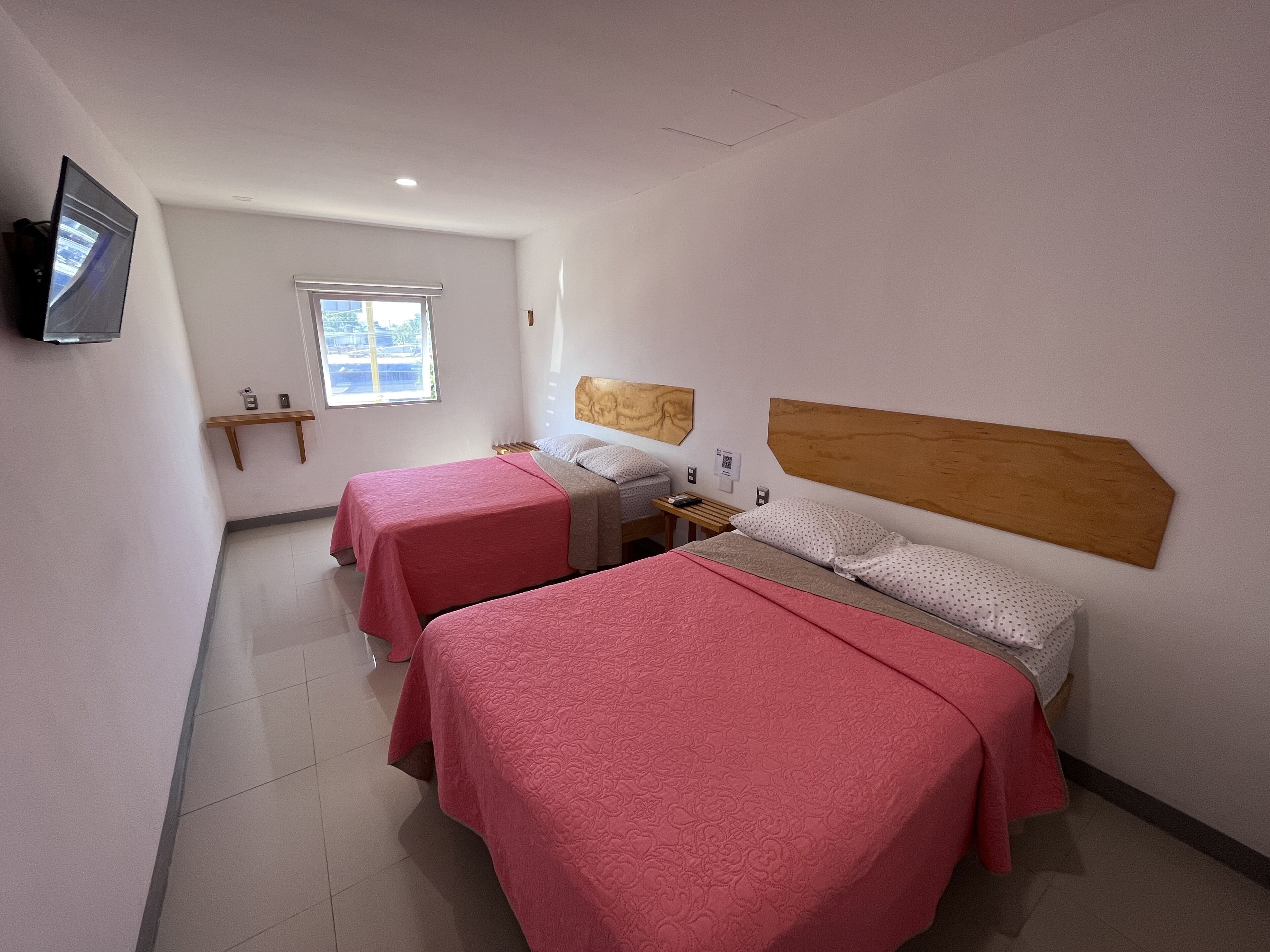 Habitación de hotel con dos camas, un televisor, una ventana y un cabecero de madera.