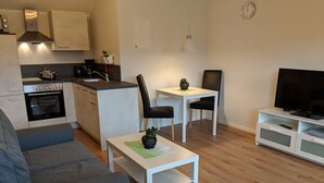 Een moderne keuken met een fornuis, oven en spoelbak. Er is een eethoek met een tafel en stoelen. Een televisie staat op een dressoir aan de rechterkant.