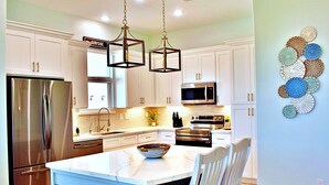 A modern kitchen with white cabinets, stainless steel appliances, and a central island with seating. - Beach Please (Surfside Beach)