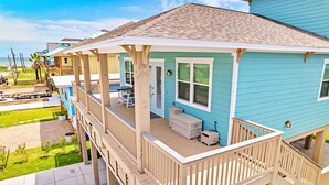 A two-story house with a covered porch, a small outdoor seating area, and a view of the ocean. - Beach Please (Surfside Beach)