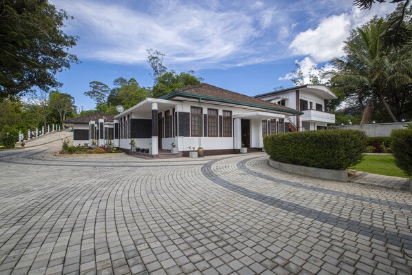 A modern building with a curved roof, a paved driveway, and surrounding greenery. - Bandarawela City Bungalow (Bandarawela)