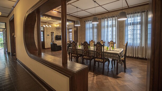 A dining area with a wooden table and chairs, a chandelier, and a view of a living room through a mirror. - Bandarawela City Bungalow (Bandarawela)