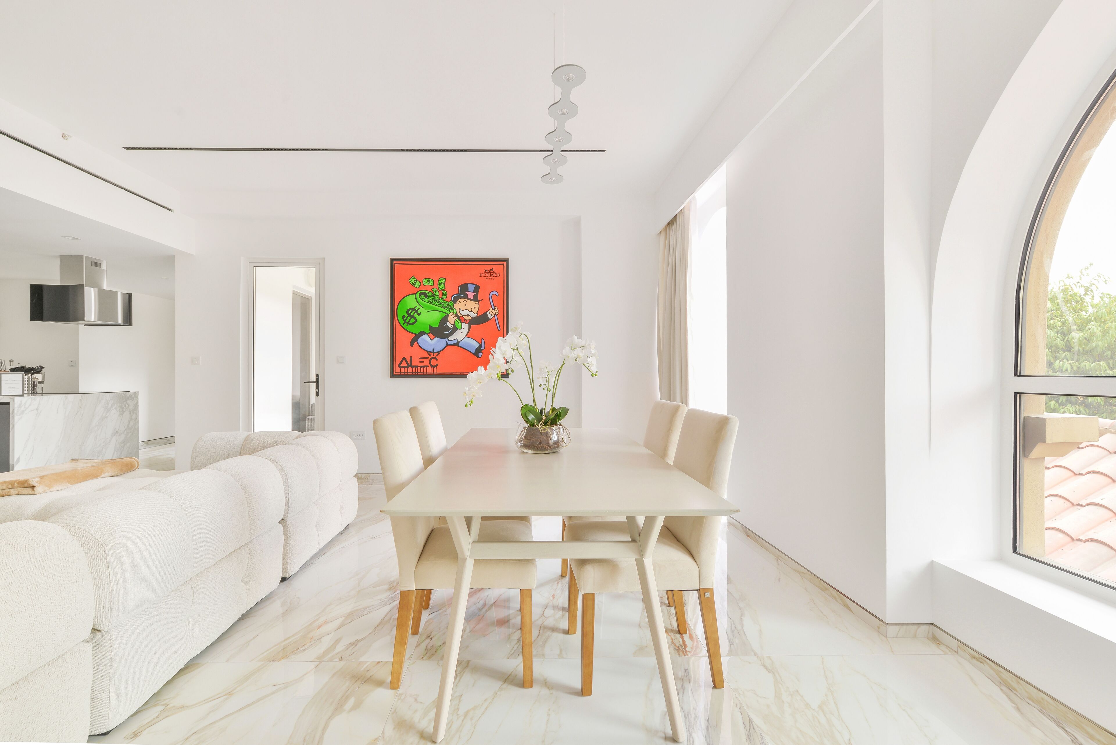 A modern dining area with a white table and chairs, a vase with flowers, and a colorful poster on the wall.