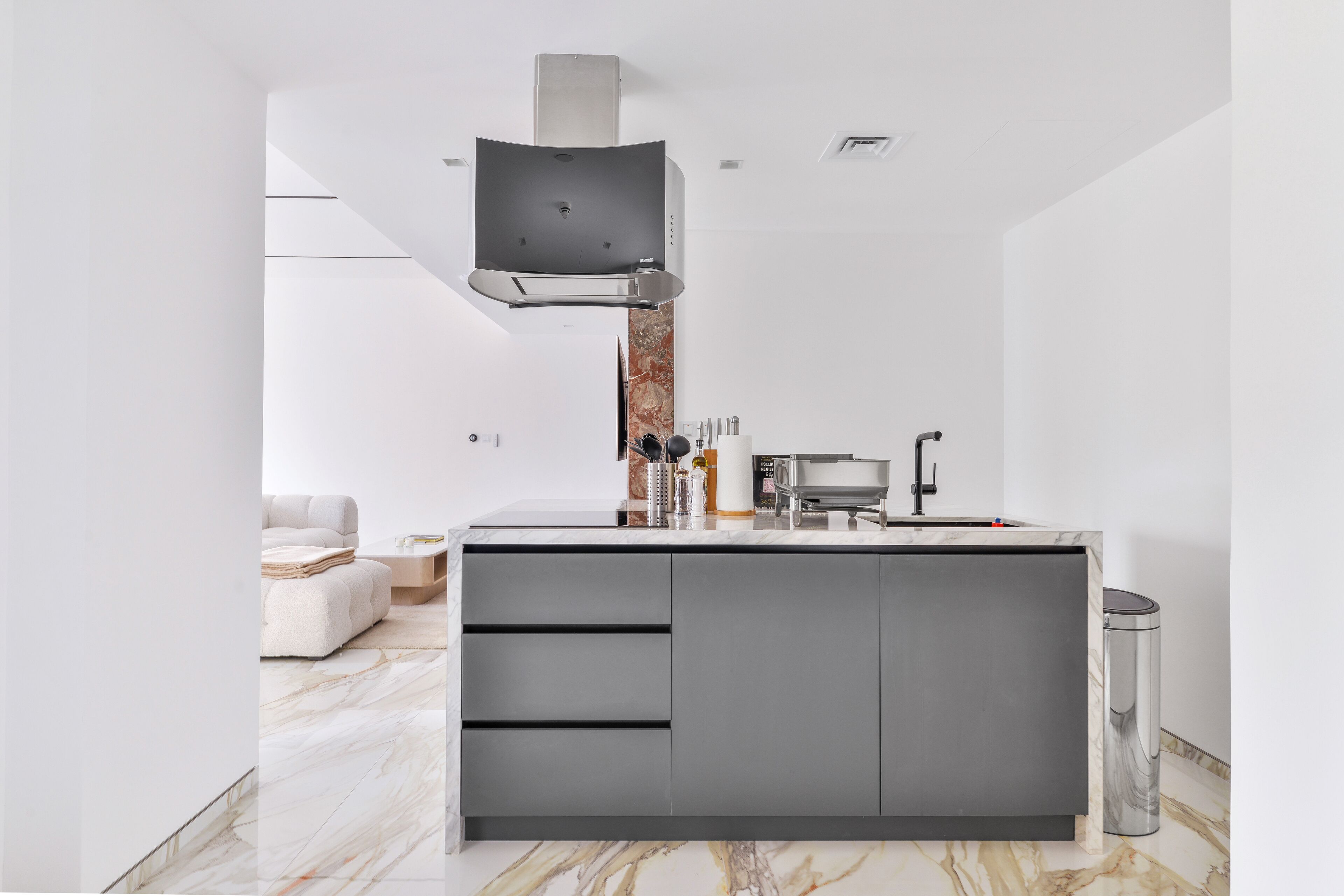 A modern kitchen with a marble countertop, built-in cabinets, and a stainless steel range hood.