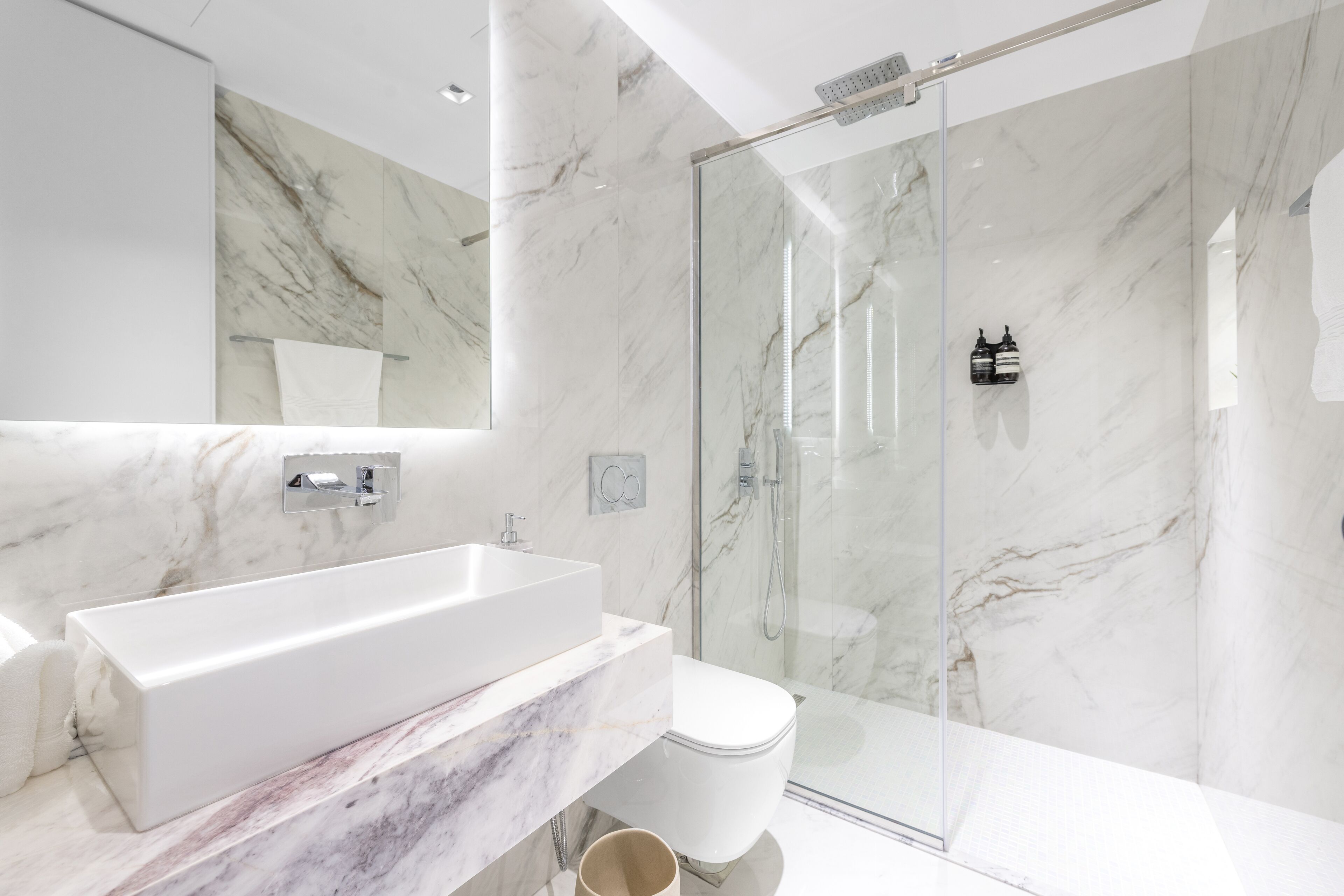 Un bagno moderno con un ampio lavandino bianco, una cabina doccia in vetro e pareti in marmo.