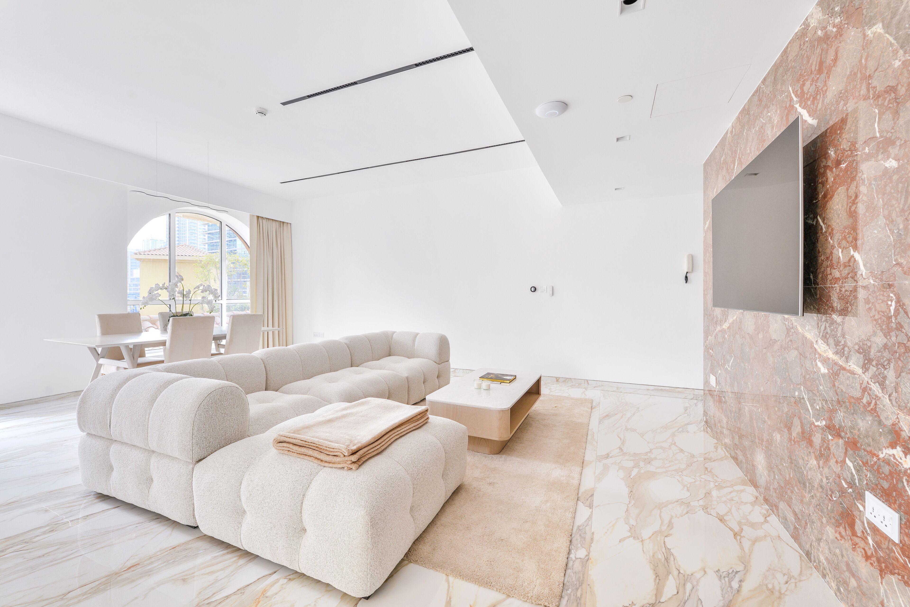 A modern living room with a sectional sofa, a coffee table, and a TV mounted on a marble wall.
