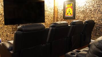 A home theater with four black leather recliner seats, a flat-screen TV mounted on the wall, and a framed poster on the wall.