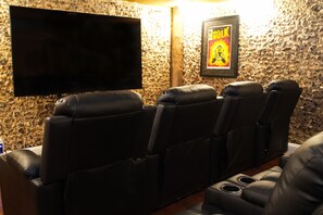 Ein Heimkino mit vier schwarzen Ledersessel, einem flachbildfernseher an der Wand und einem gerahmten Poster.