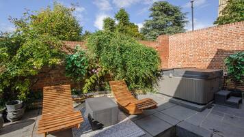 Un patio con sillones de madera, un jacuzzi y un muro de ladrillo.
