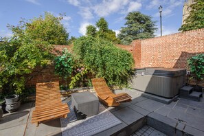 Eine Terrasse mit Holzliegen, einem Whirlpool und einer Backsteinmauer.