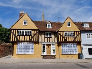 A traditional Tudor-style house with a symmetrical facade, two chimneys, and a central door with a small porch.