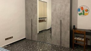 Quarto com guarda-roupa, uma mesinha com cadeira e parede com um desenho circular.