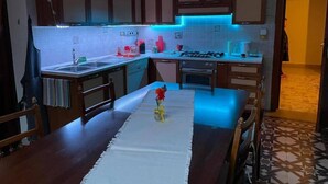Uma cozinha compacta com armários de madeira, painel de azulejos, mesa de jantar com cadeiras e uma pequena planta decorativa.