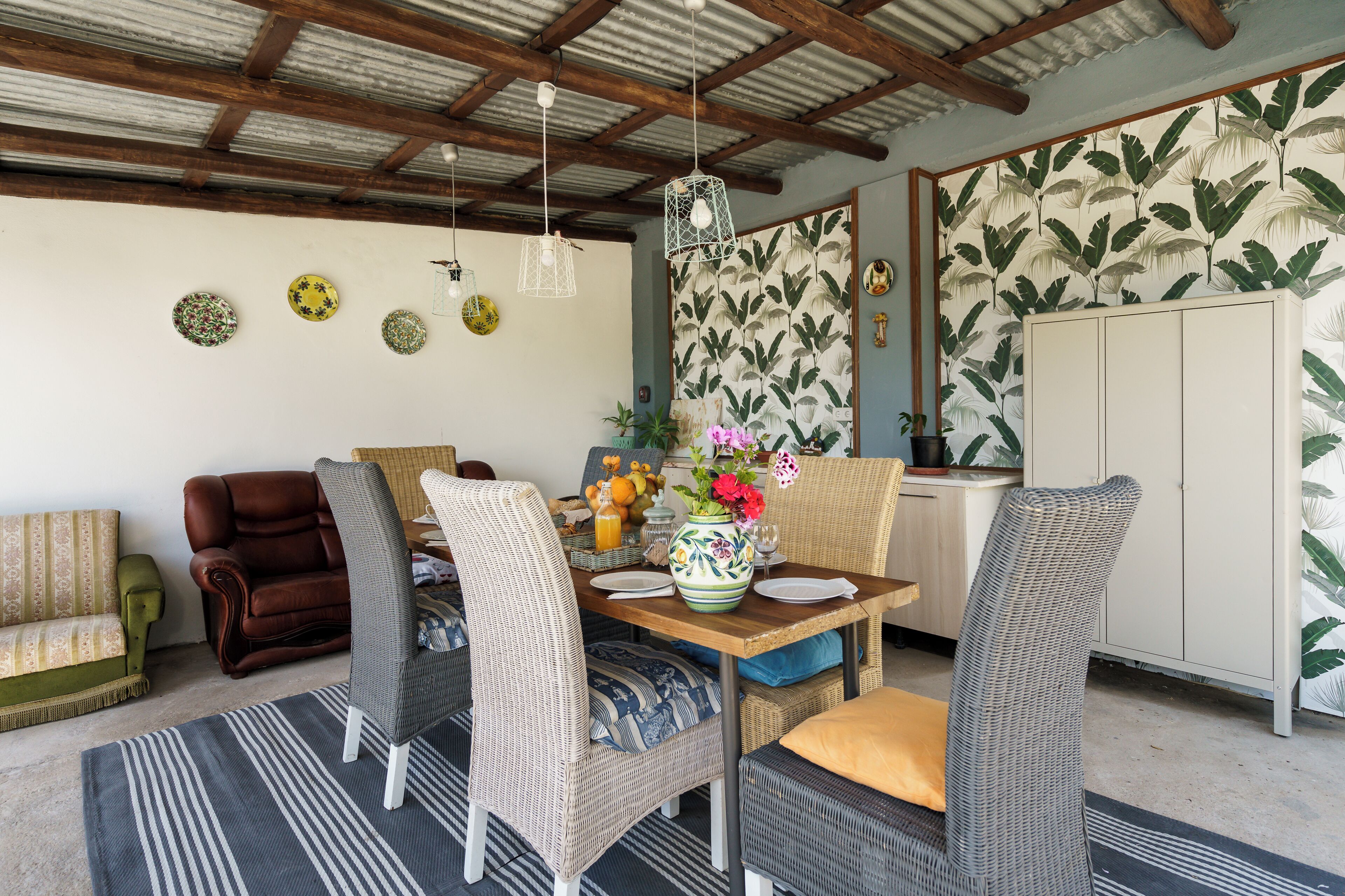 A dining area with wicker chairs, a wooden table, and hanging light fixtures.