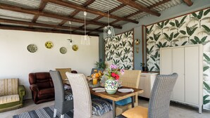 Een eethoek met rieten stoelen, een houten tafel en hangende lampen.
