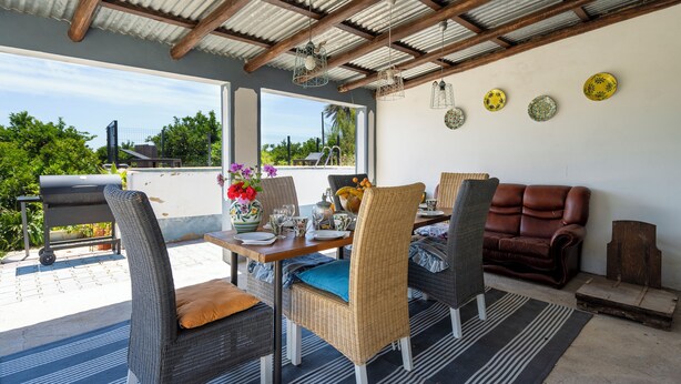 Een terras buiten met rieten meubels, een barbecue en decoratieve borden aan de muur.