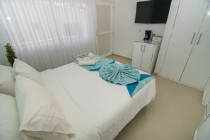 A hotel room with a bed, a TV mounted on the wall, a wardrobe, and a small table with a coffee maker.