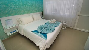 Habitación de hotel con una cama, una mesita de noche, una ventana con cortinas translúcidas y un mural en la pared.