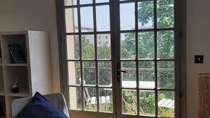 Ein Zimmer mit einer großen Schiebetür zum Außenbereich, ein Sessel mit blauer Sitzkissen, ein weißes Regal und ein Korbwäschekorb.