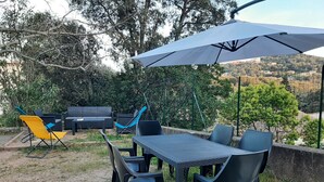Eine Terrasse im Freien mit Tisch und Stühlen, einem gelben Klappstuhl und einem großen Sonnenschirm, der Schatten spendet.
