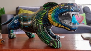 Una detallada escultura de león sobre una mesa de madera en una habitación con un sofá y cojines al fondo.