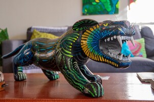 Una detallada escultura de león sobre una mesa de madera en una habitación con un sofá y cojines al fondo.