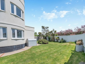 A modern building with a curved facade, a well-maintained lawn, and a stone wall with vegetation.